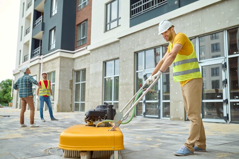 Maintenance worker power washing a sidewalk outside a commercial building